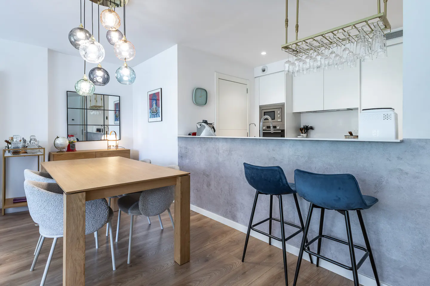 Modern dining area with a wooden table, textured grey chairs, blue bar stools, and a contemporary glass pendant light.