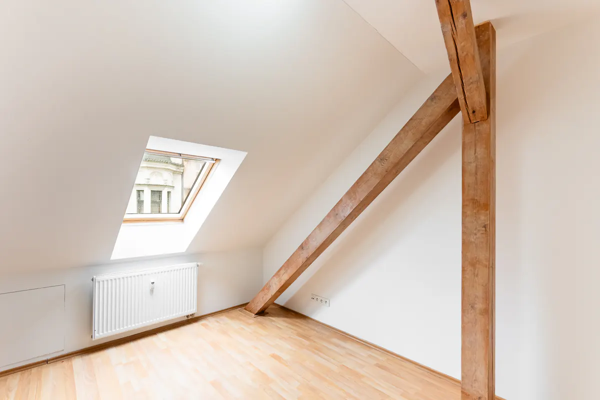 Attic room with white walls, wood floor, exposed beams, and a skylight window. A radiator sits below the window.