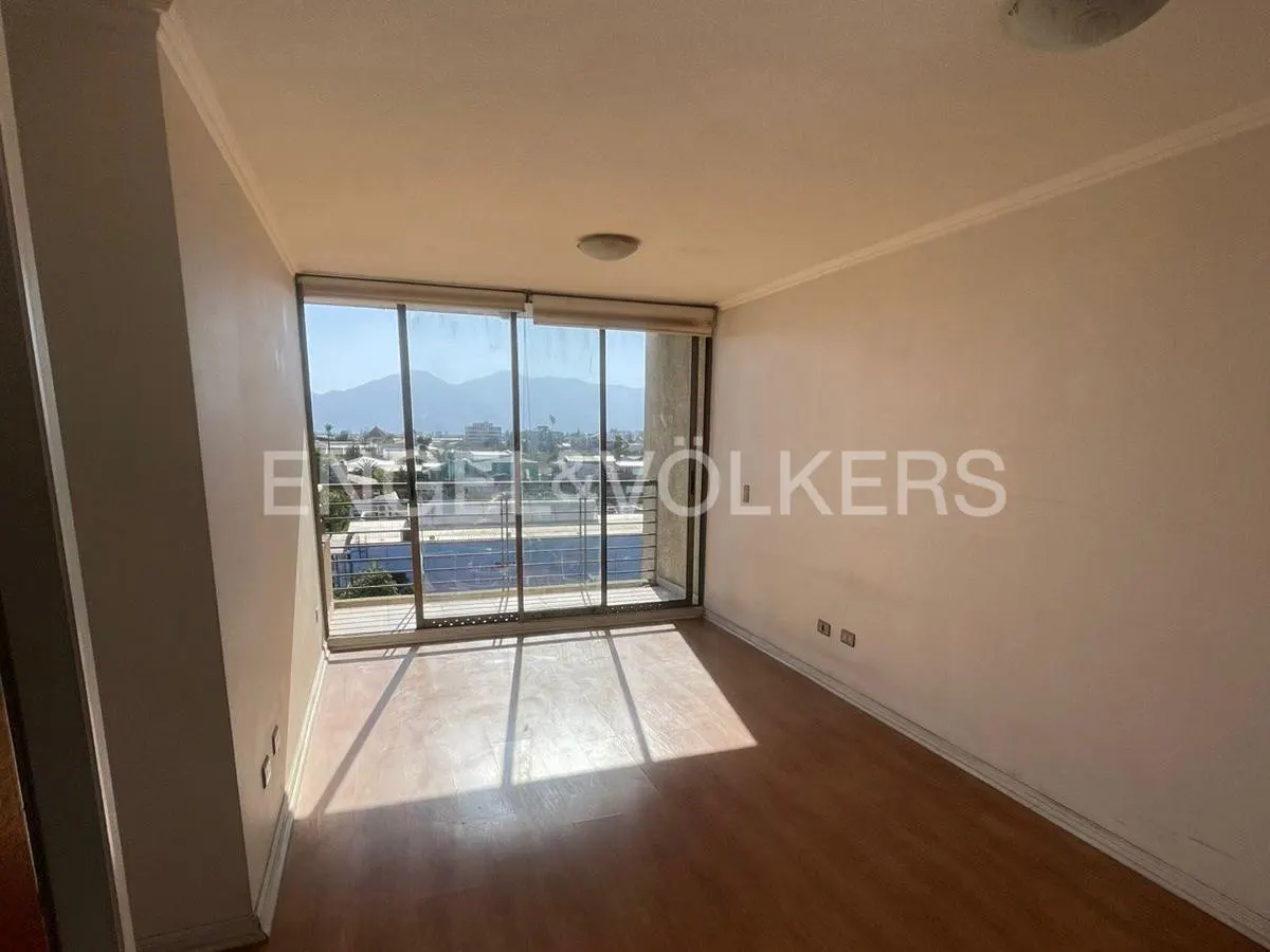 Empty room with wood floors, white walls, and large sliding glass doors to a balcony with a city and mountain view.