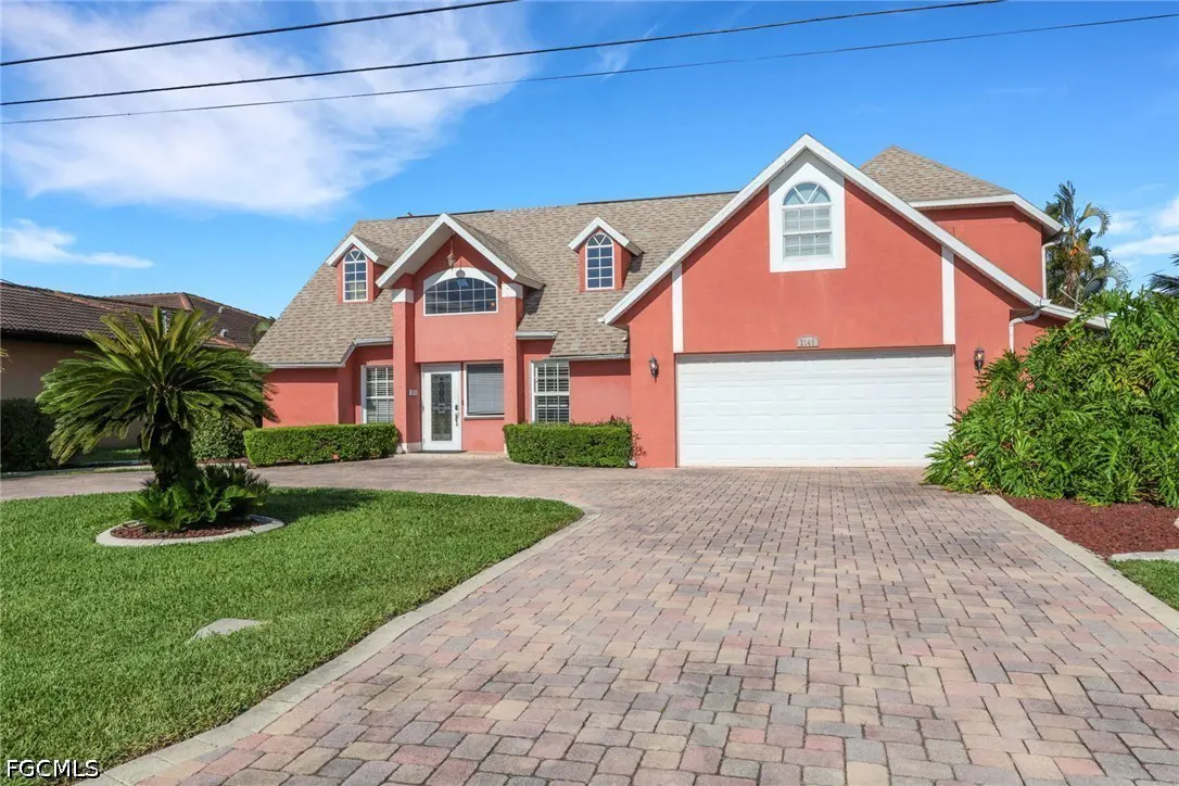 Two-story coral house with a white garage door and trim, a brick driveway, and a green lawn.