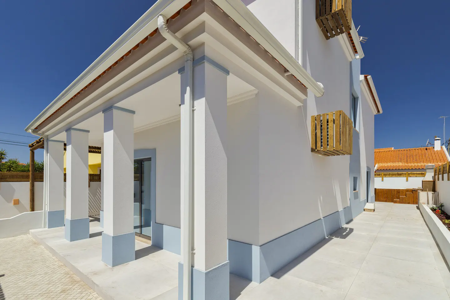 Exterior view of a white house with a covered porch, light blue trim, and wooden AC unit covers against a clear blue sky.