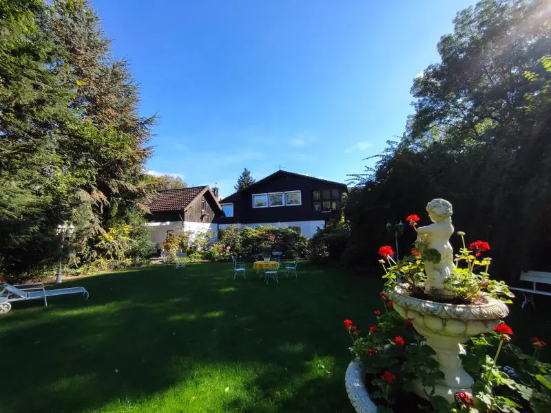 A house with a large green lawn, trees, and a fountain with red flowers.