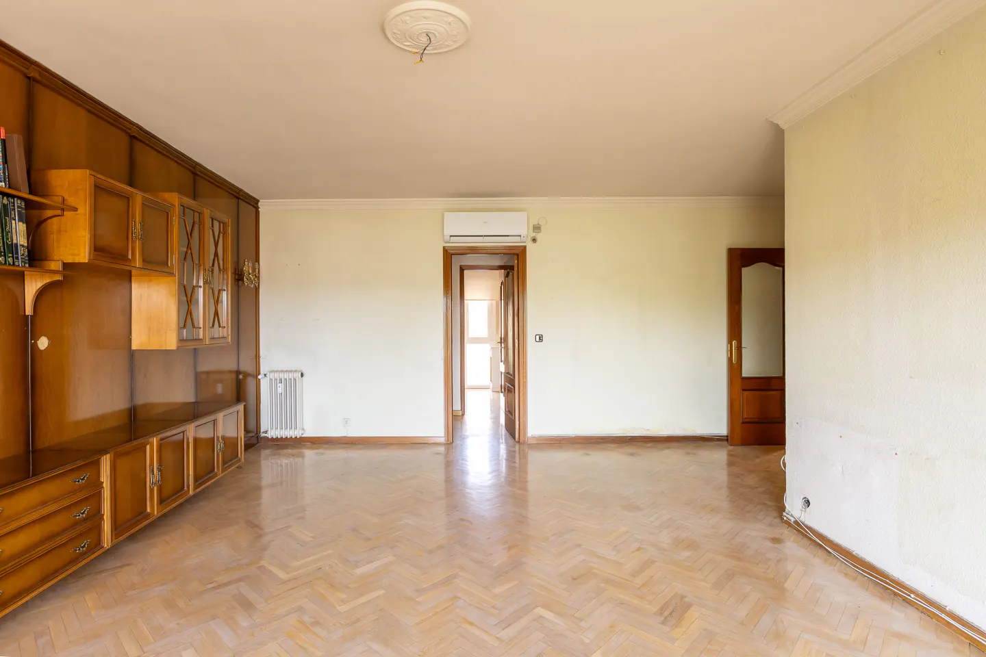 A bright, empty living room with wood floors, a built-in cabinet, and two doorways.