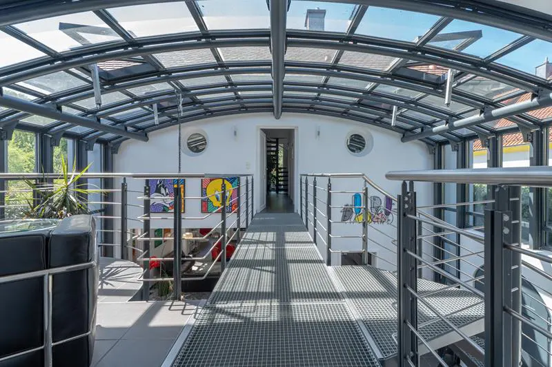 Interior view of a modern walkway with a glass roof, metal railings, and colorful cartoon art on the white walls.