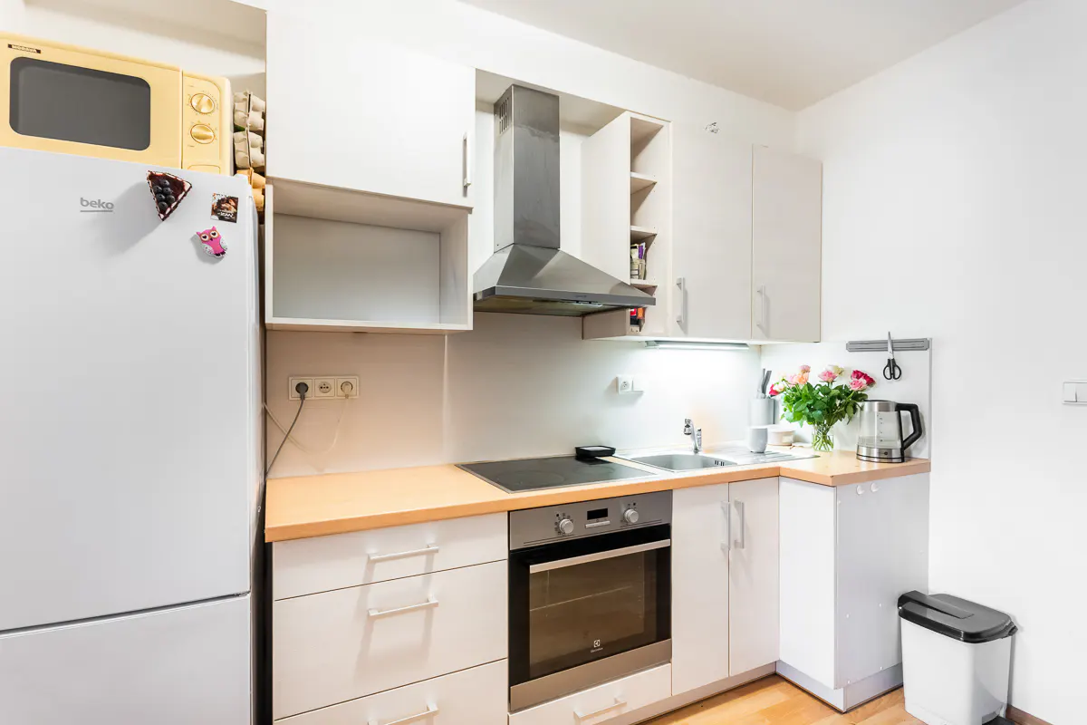 Bright kitchen with white cabinets, stainless steel appliances, and light wood countertops. A yellow microwave sits atop a white refrigerator.