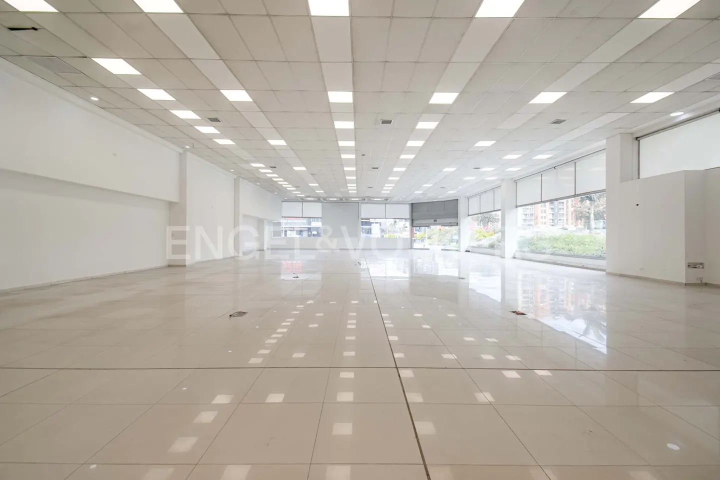 Bright, empty commercial space with white walls, tile floor, and large windows with roller shades.