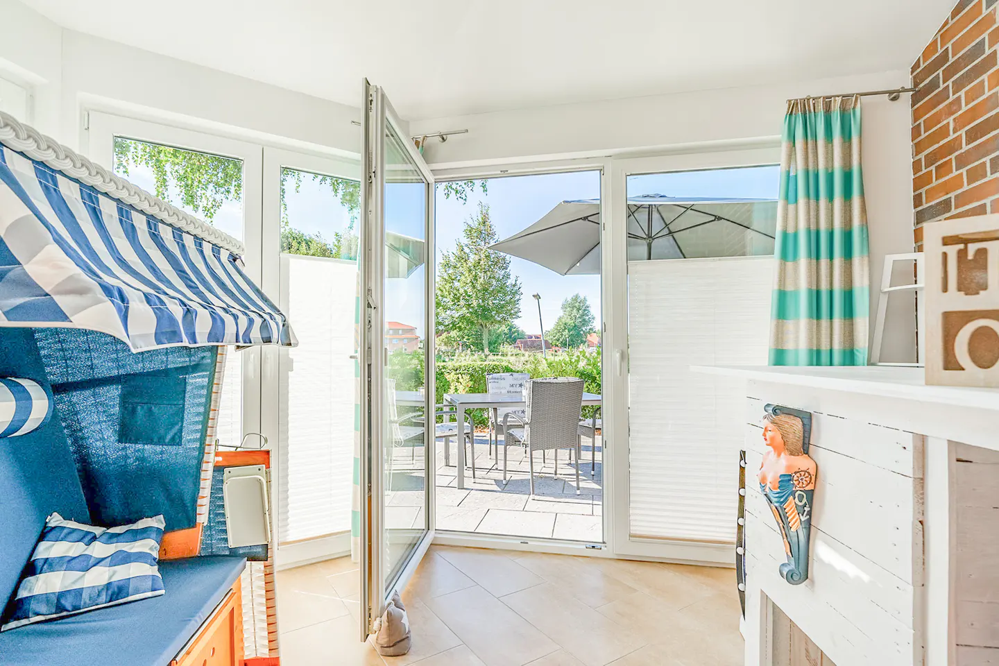 Bright sunroom with open glass doors leading to a patio. A blue and white striped beach chair sits inside.