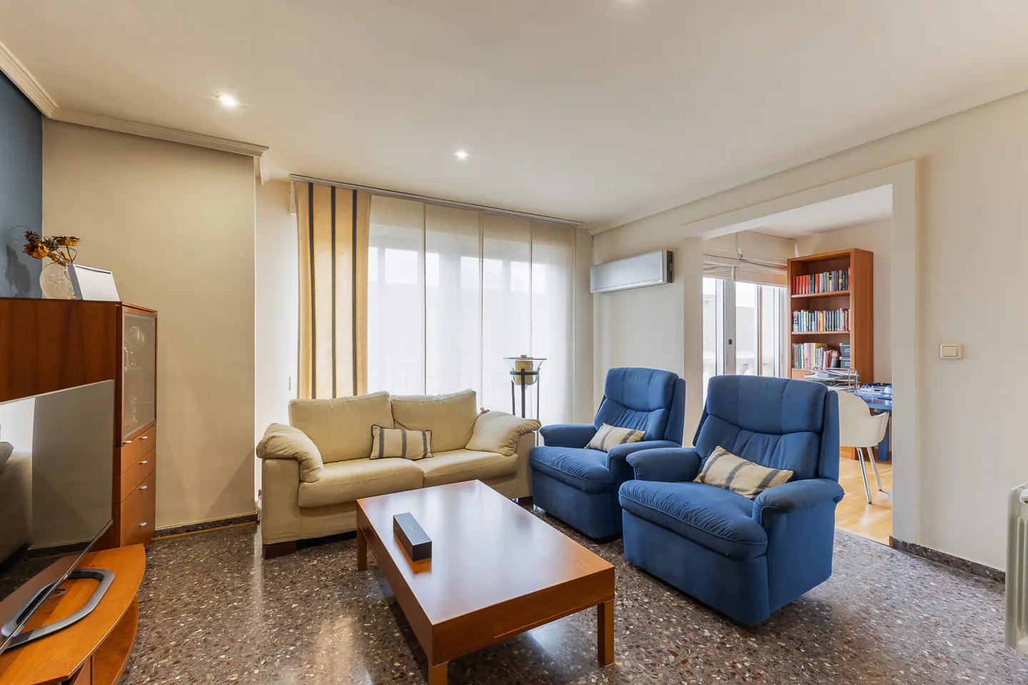 A living room with a beige sofa, two blue armchairs, and a wooden coffee table on a speckled floor.
