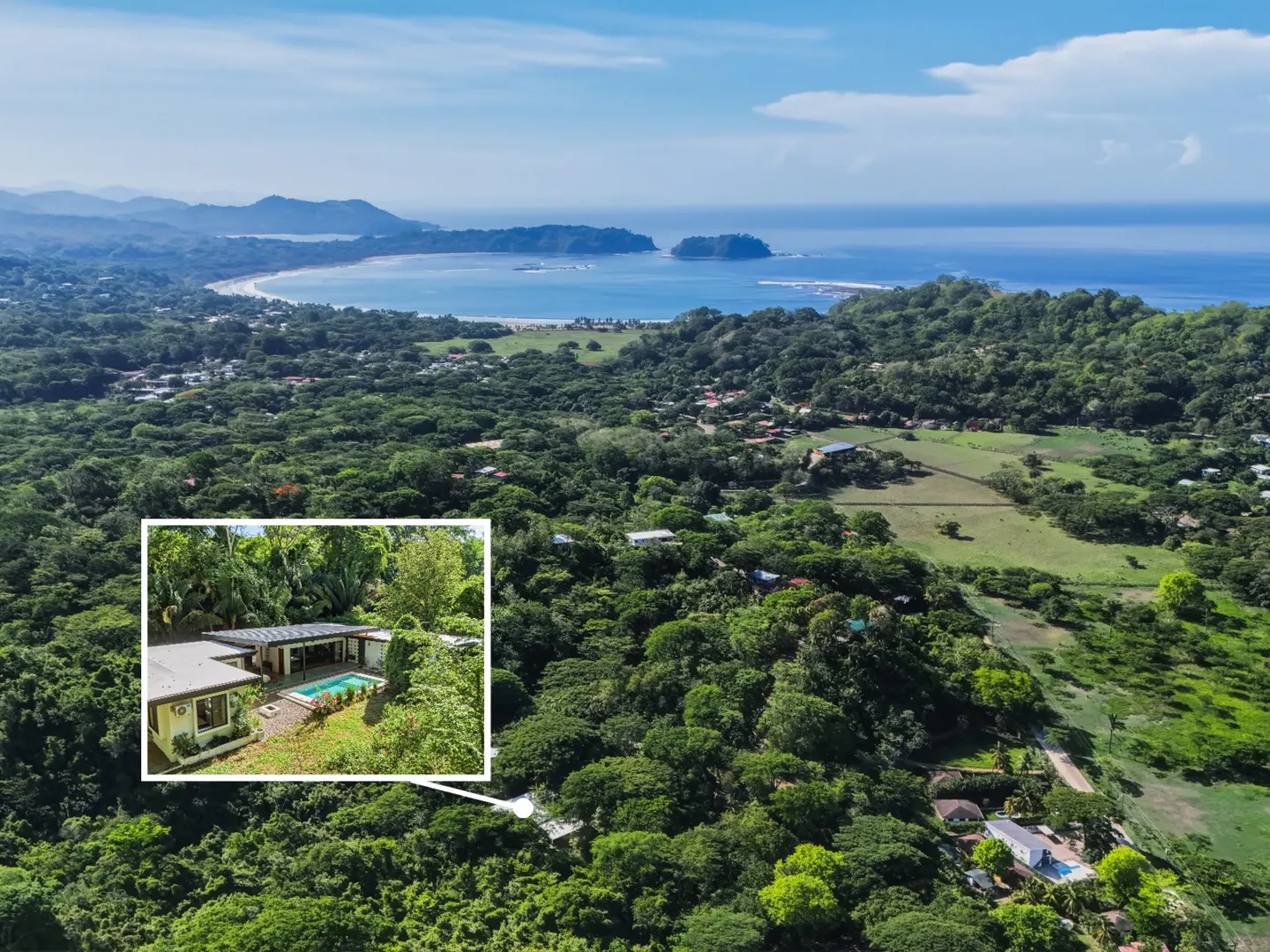 Aerial view of a house with a pool in a lush, green landscape near a beach and ocean.