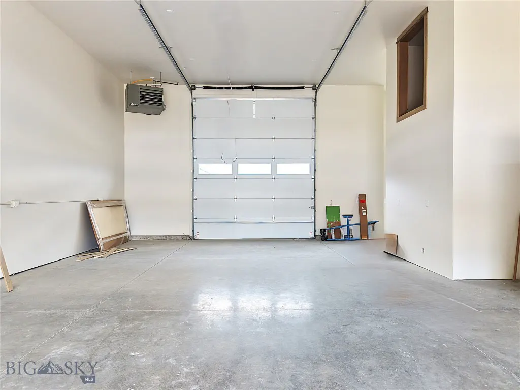 A bright, empty garage with white walls, a concrete floor, and a closed white garage door.