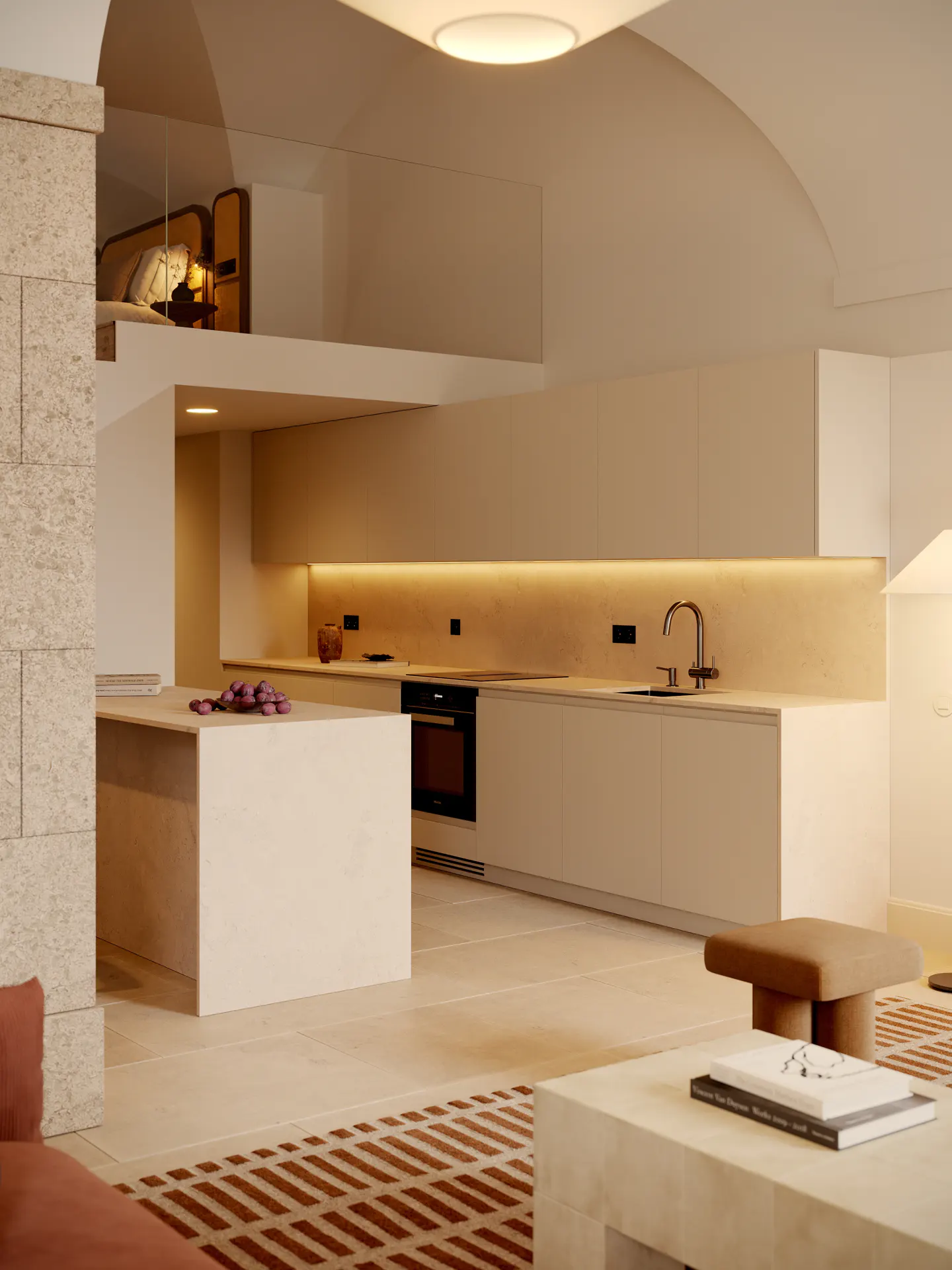 Modern kitchen with light beige cabinets, island with fruit, and a loft bedroom above. Warm lighting and a patterned rug add to the cozy atmosphere.
