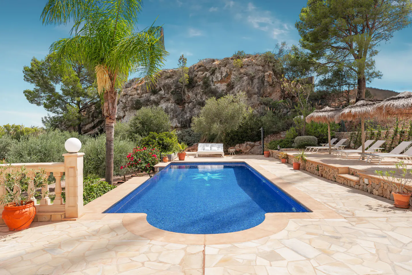 Outdoor pool with blue tiles and a star design, surrounded by stone patio, palm tree, and lounge chairs.