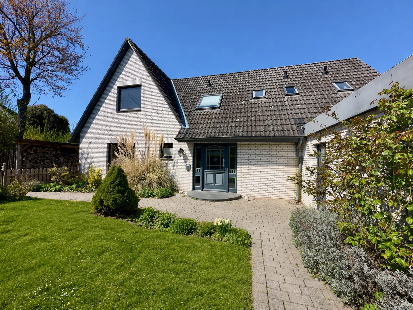 Exterior of a white brick house with a gray roof, blue door, green lawn, and blue sky.