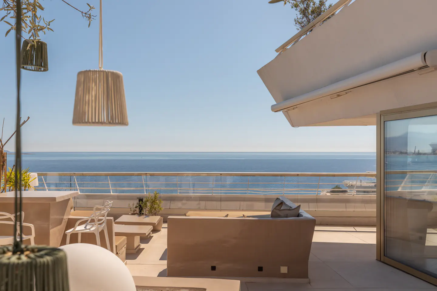 Luxury patio with ocean view. Beige furniture, white awning, and hanging lamps create a relaxing outdoor space.