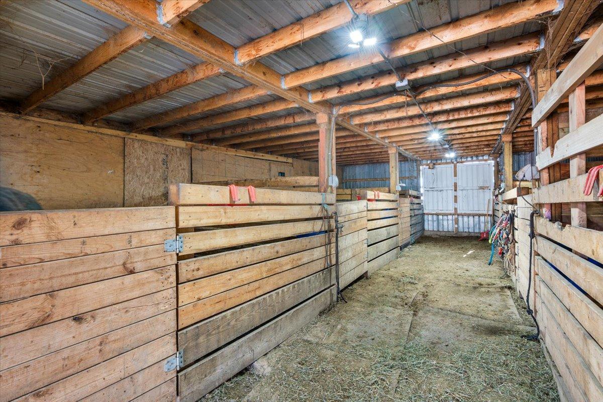 Interior of a rustic horse stable with wooden stalls, a dirt floor, and overhead lighting.