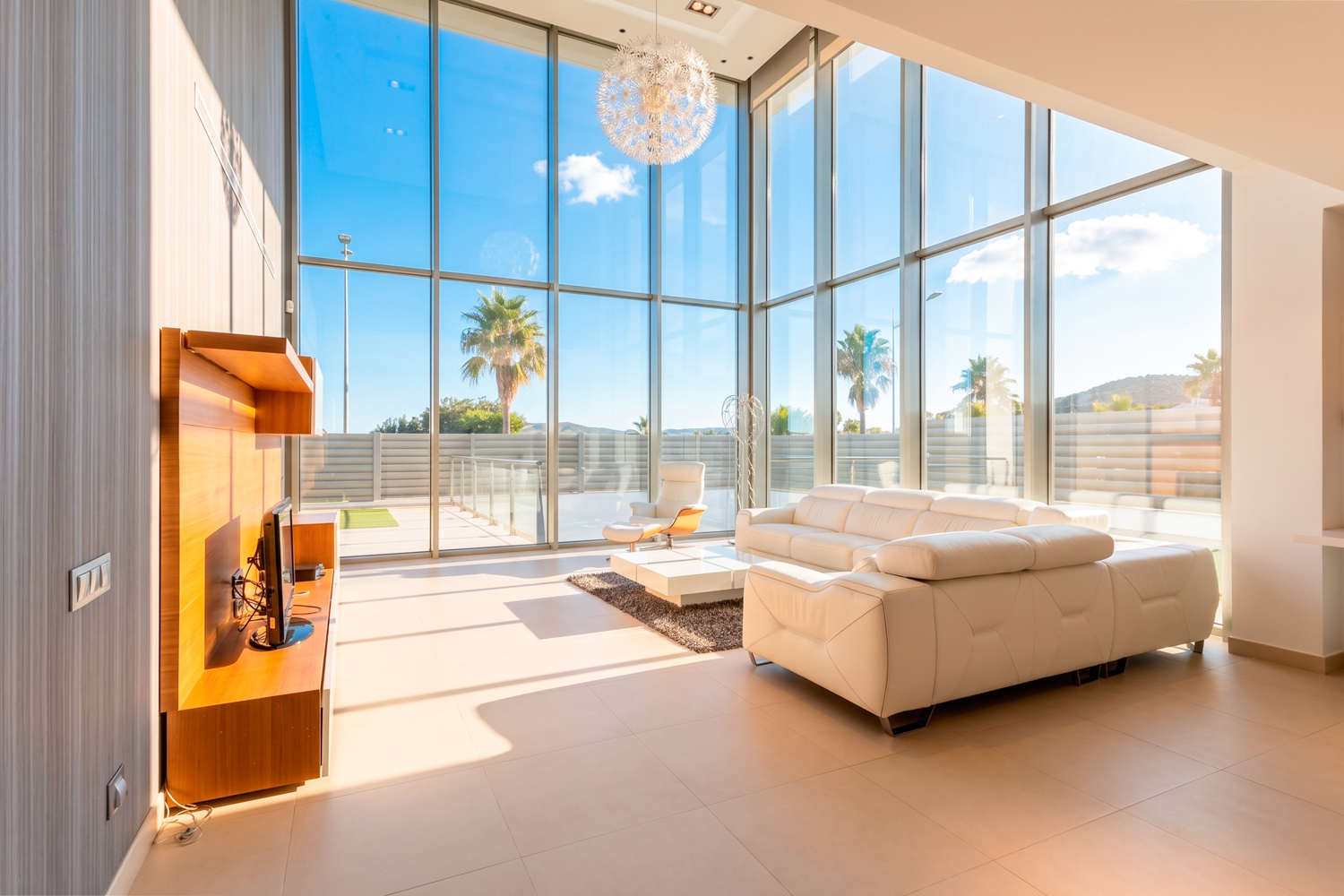 Modern living room with white leather sofa, floor-to-ceiling windows, and a view of palm trees under a bright blue sky. [AI-generated text]