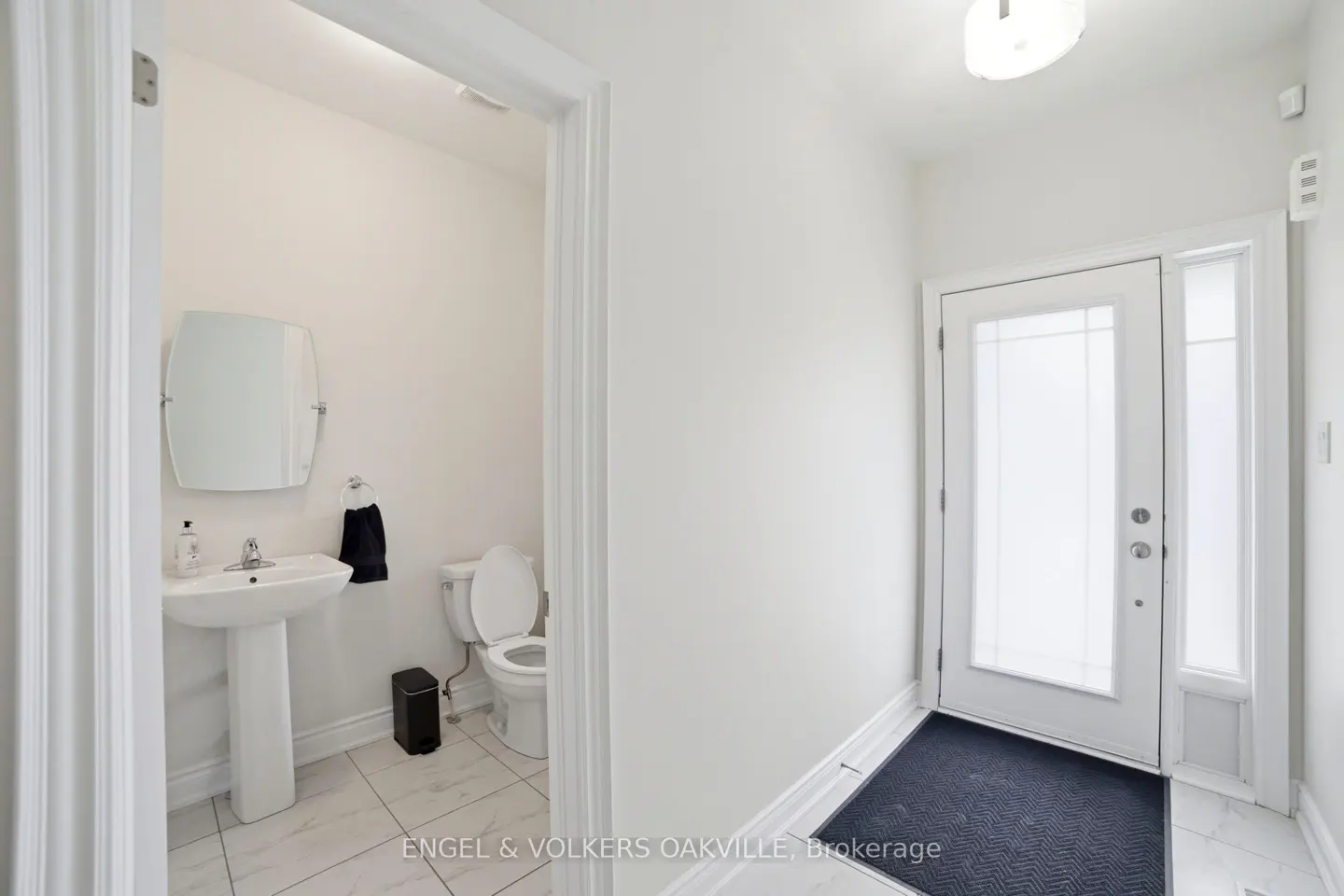 Bright, white foyer with a powder room visible through an open doorway. A white door with glass panels is on the right.