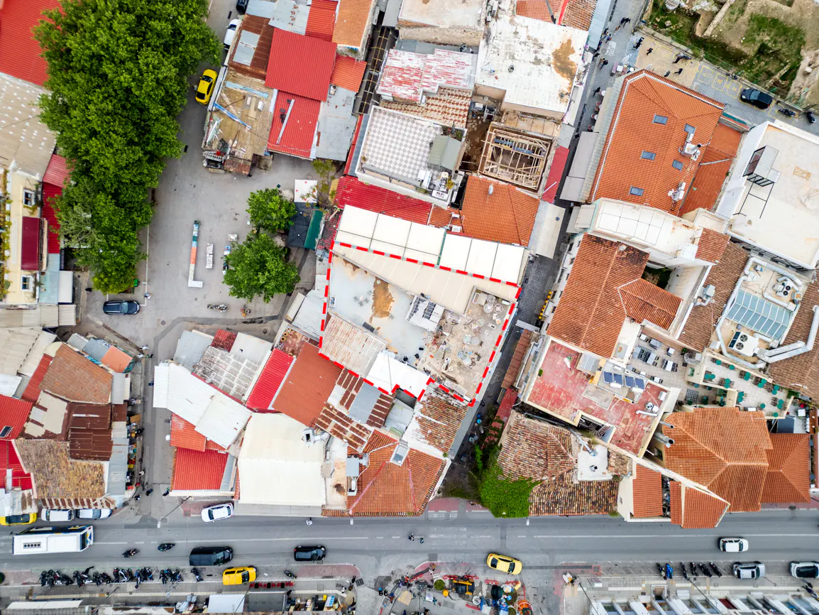 Aerial view of a European city with red-tiled roofs, a building outlined in red, and a busy street below.