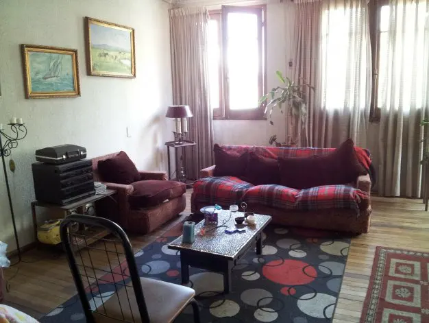 Living room with a red plaid sofa, armchair, and a black coffee table on a patterned rug. Two framed paintings hang on the wall.