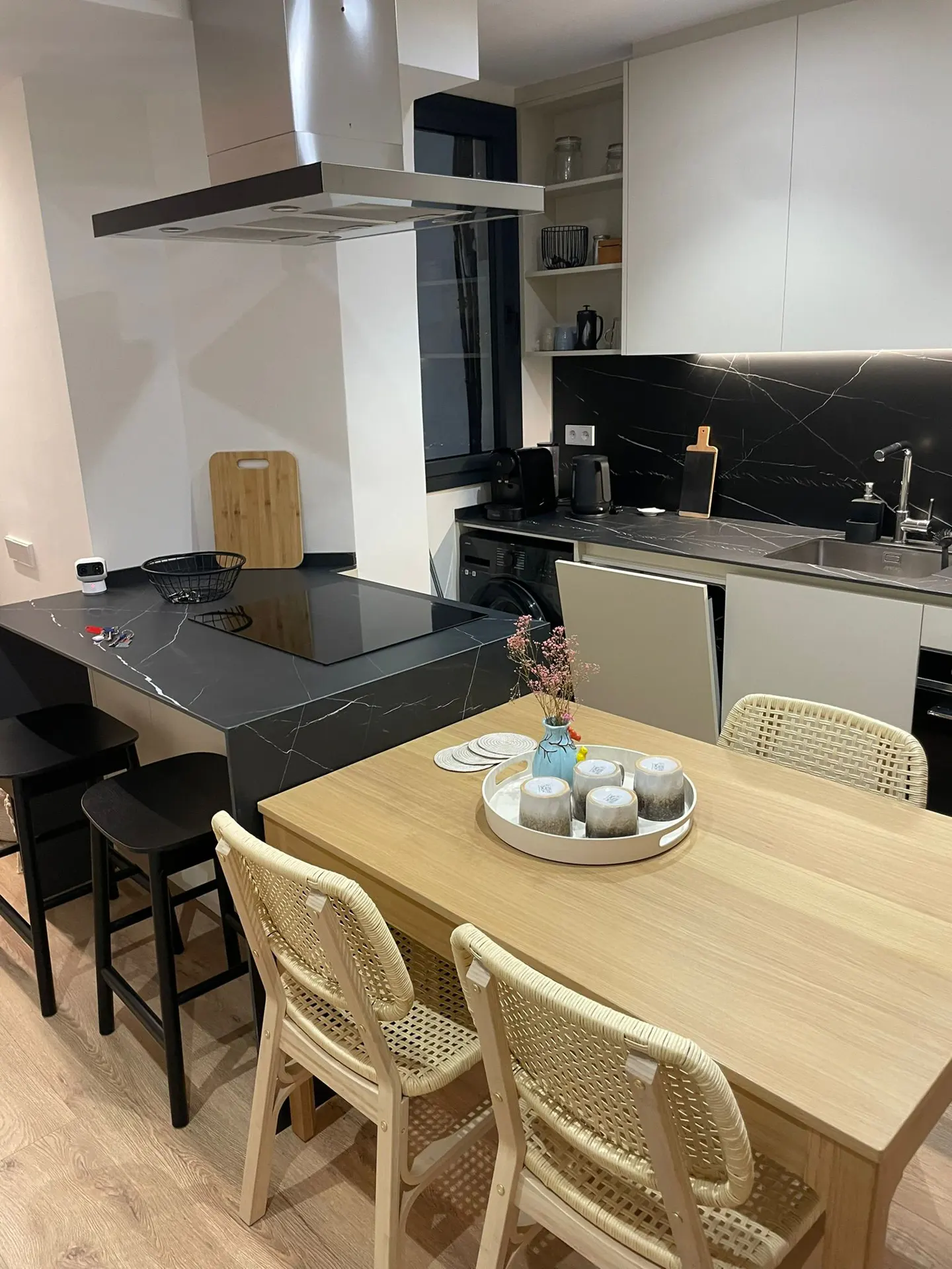 Modern kitchen with a wooden dining table, woven chairs, and a black marble island featuring a built-in stovetop.
