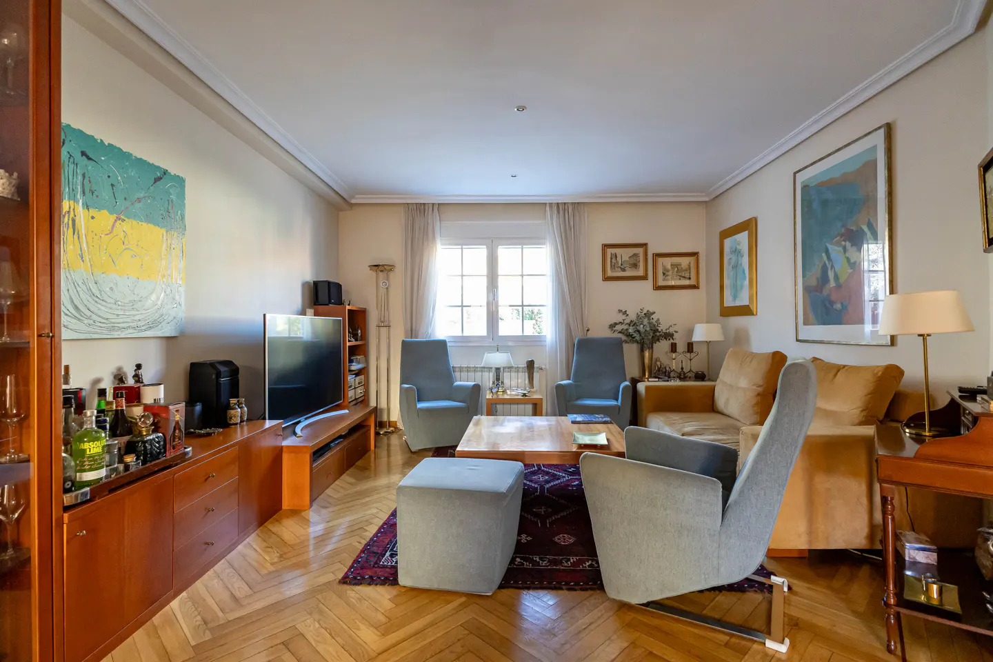 Cozy living room with light wood floors, blue armchairs, a tan sofa, a wooden coffee table, and a TV on a wooden cabinet.