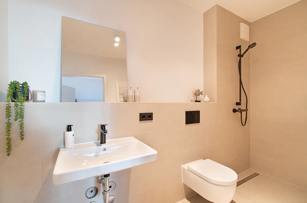 Modern bathroom with beige tiles, a white sink, a black faucet, a toilet, and a black shower head.