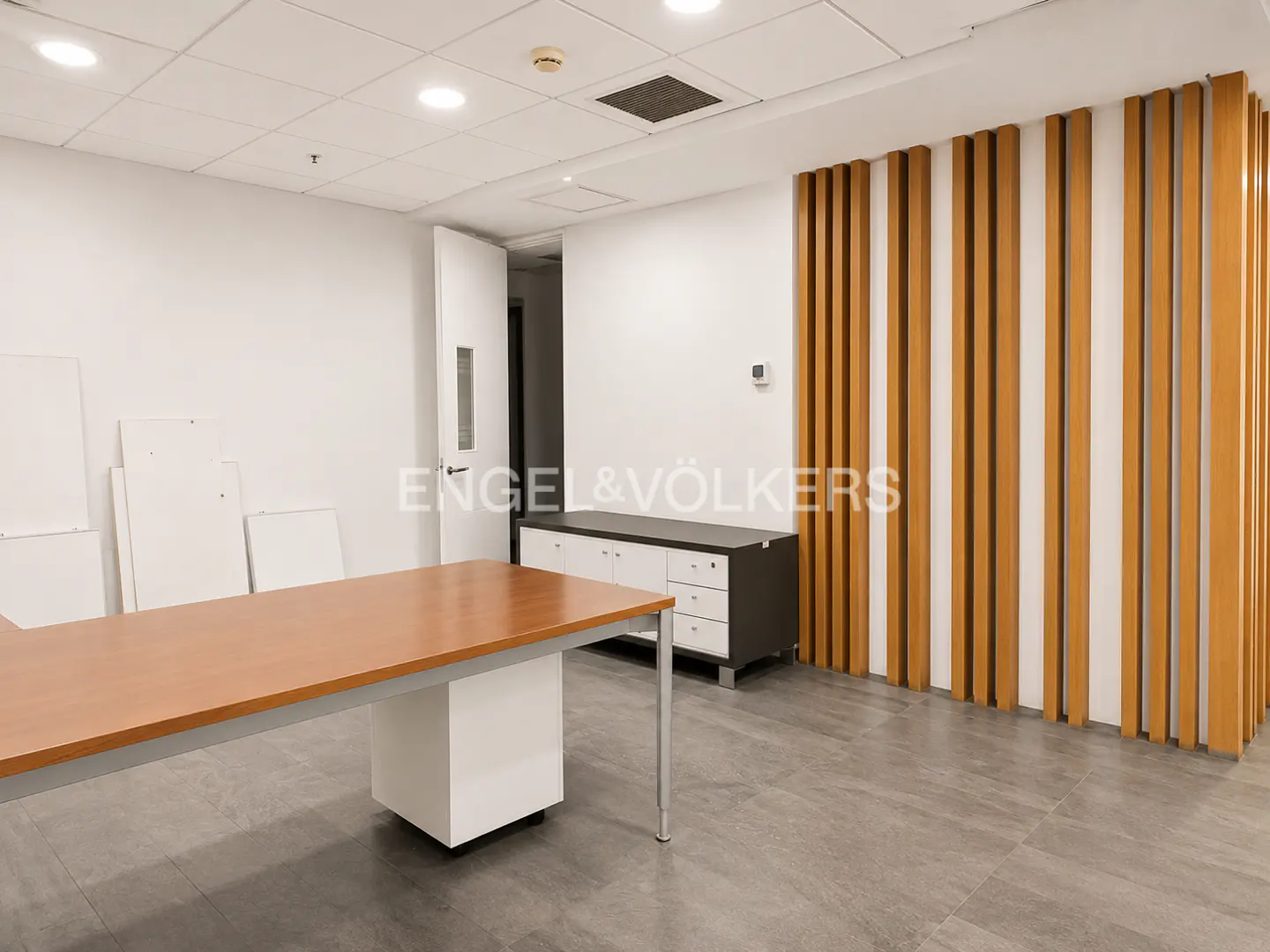 A bright office space with a long brown table, white walls, and a decorative wood slat wall.