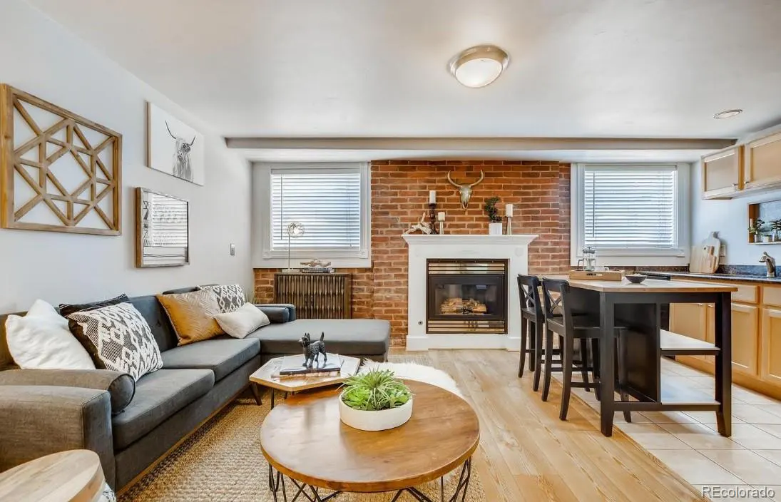 Living room with gray sectional sofa, wood coffee tables, brick fireplace, and kitchen island with bar stools.