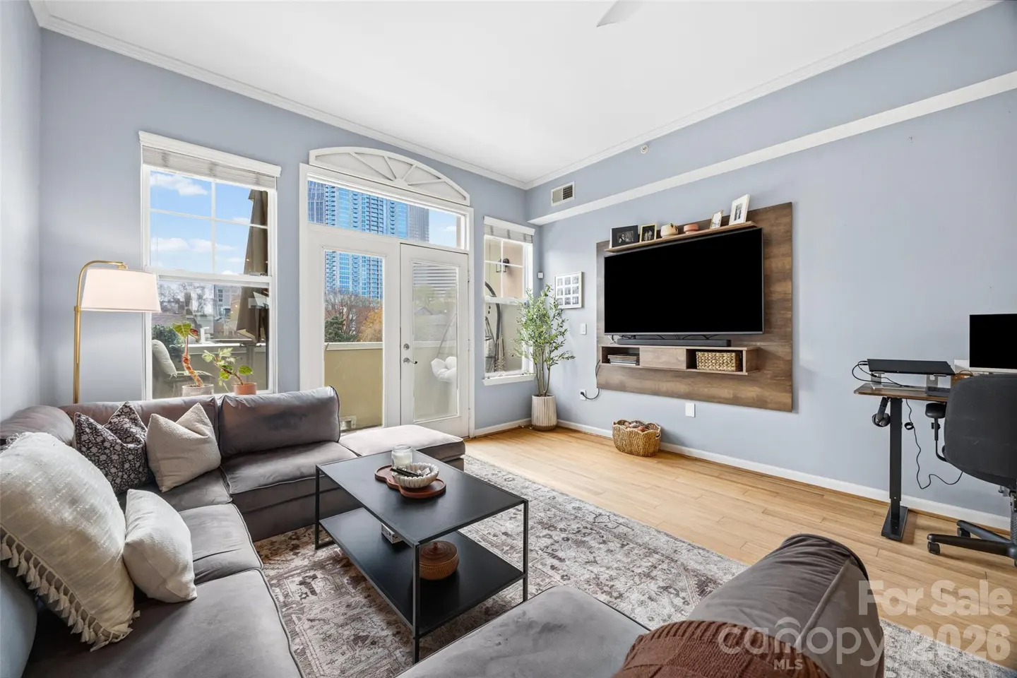Modern living room with light blue walls, gray sectional sofa, black coffee table, wall-mounted TV, and a home office desk.