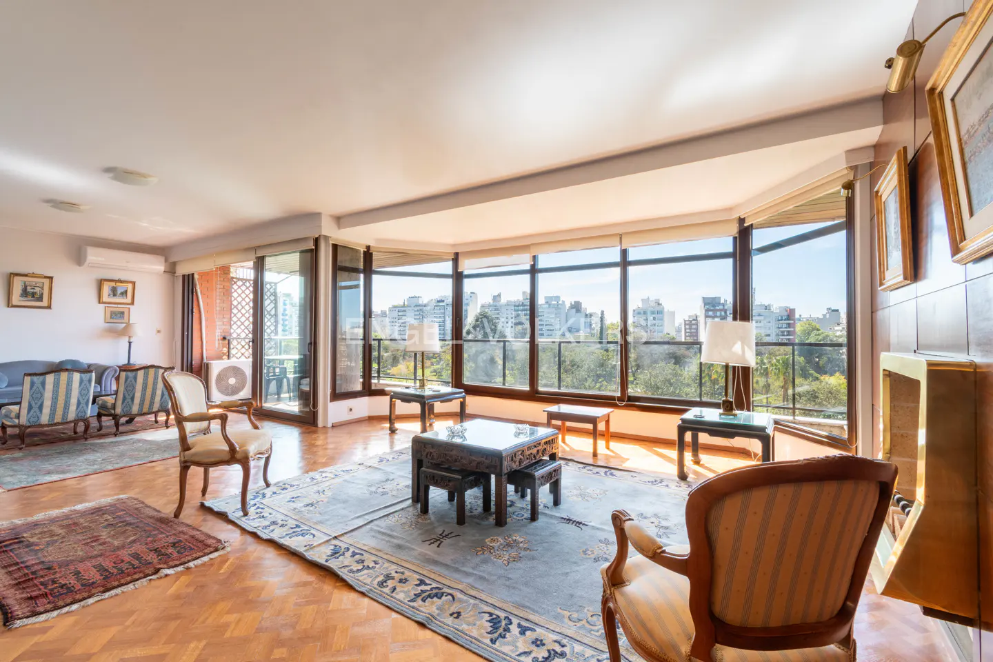 Bright living room with hardwood floors, large windows overlooking a cityscape, and antique furniture.