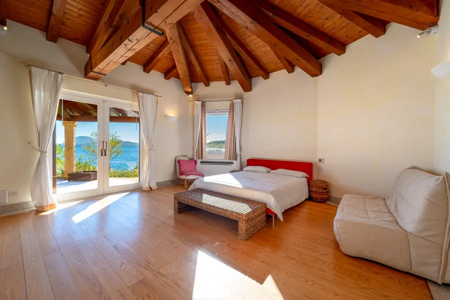 Bedroom with wood floors, exposed wood beam ceiling, and a red headboard bed. French doors open to a patio with ocean views.