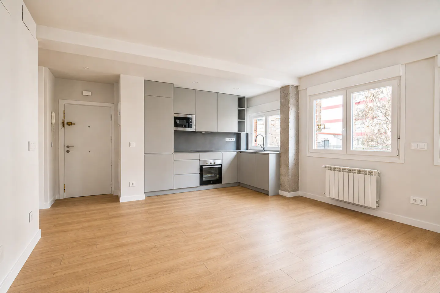Modern kitchen with light gray cabinets, stainless steel appliances, and wood-look flooring in an open-plan apartment.