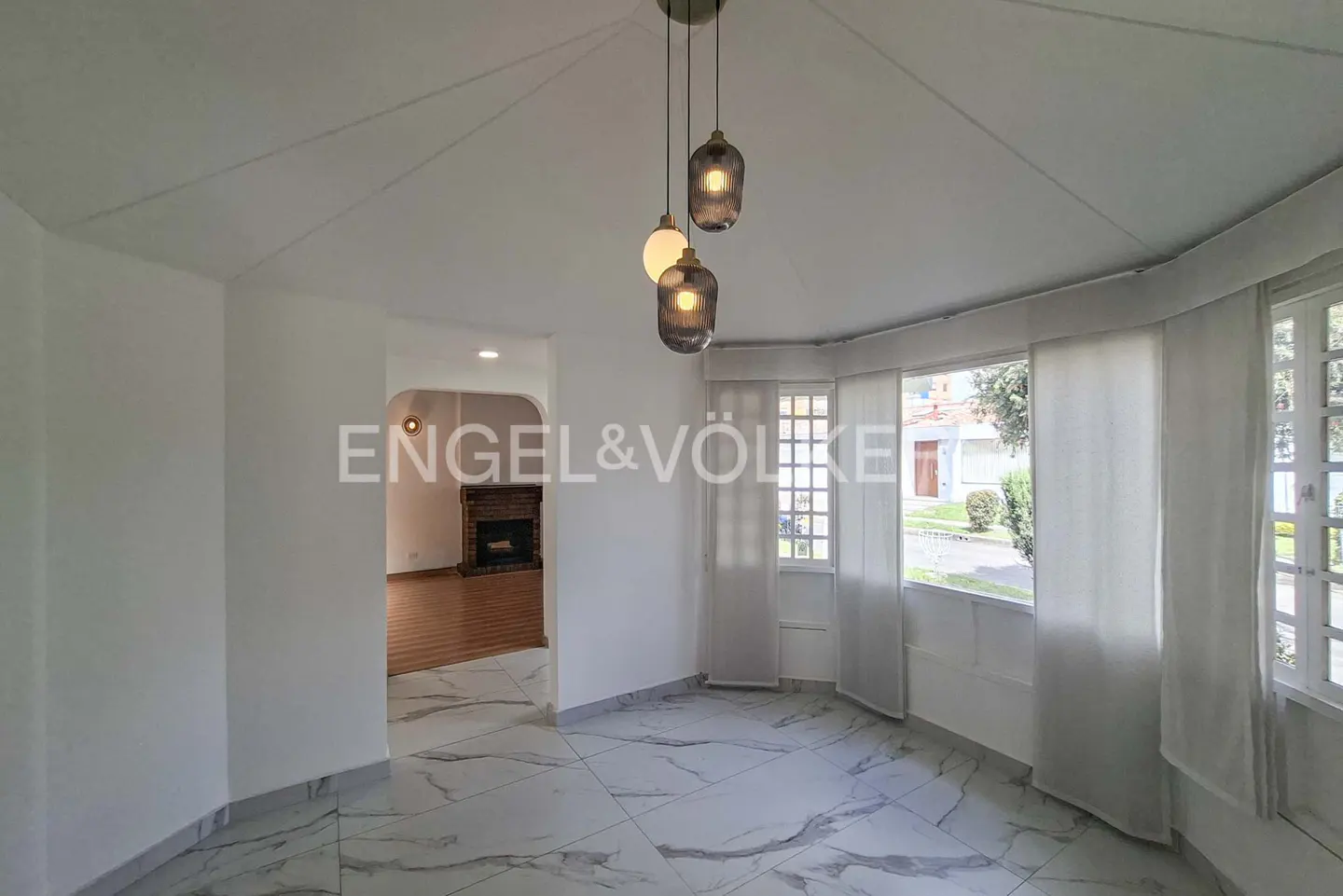 Bright room with white marble-patterned floors, modern pendant lights, and large windows looking out to a garden.