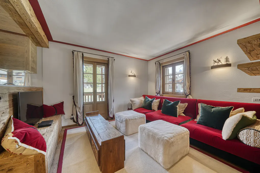 Living room with red sectional sofa, white ottomans, and rustic wood accents. A door leads to a balcony.