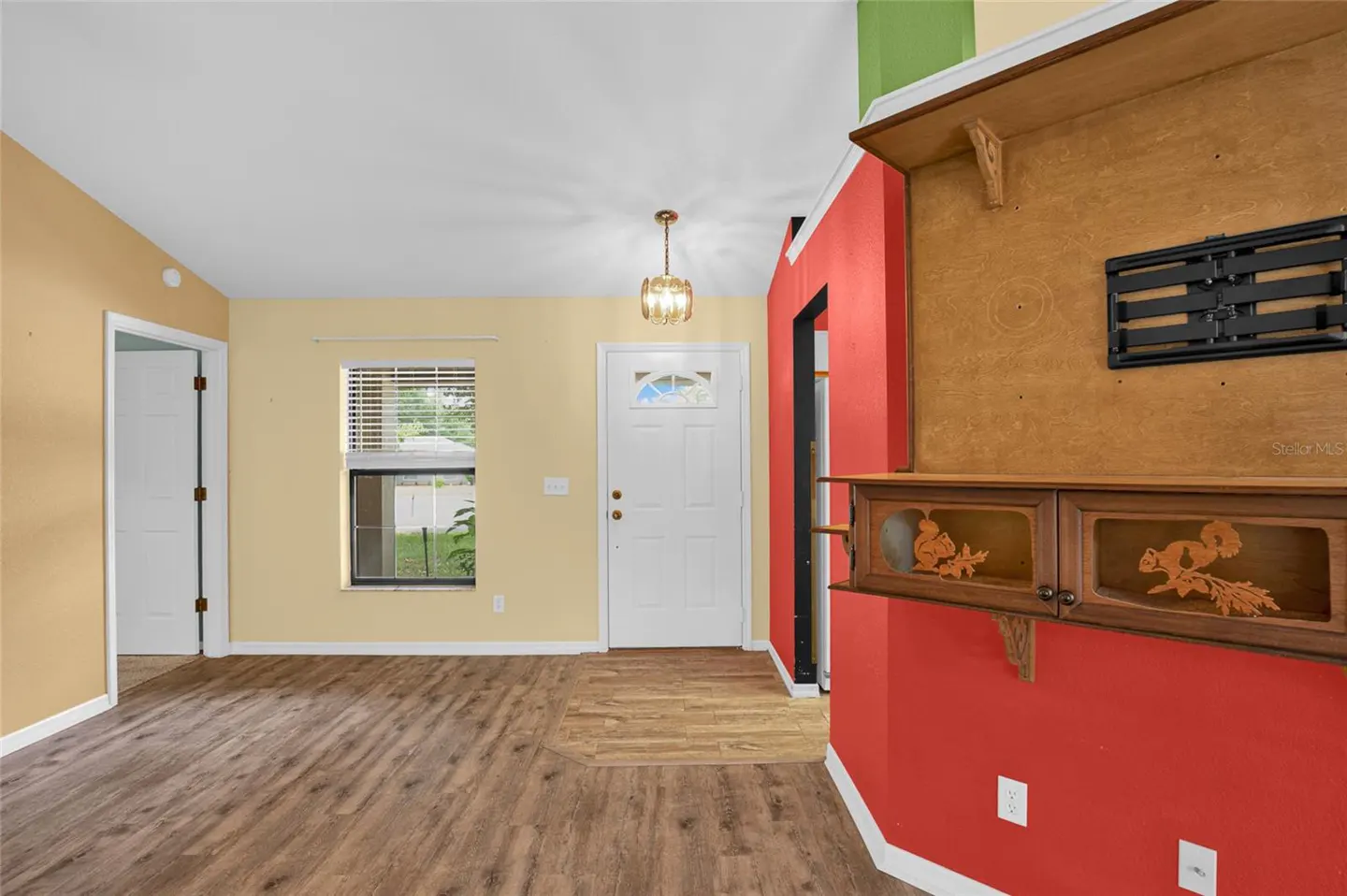 A home's interior with wood floors, yellow walls, and a white front door. A red wall features a wooden cabinet with squirrel carvings.