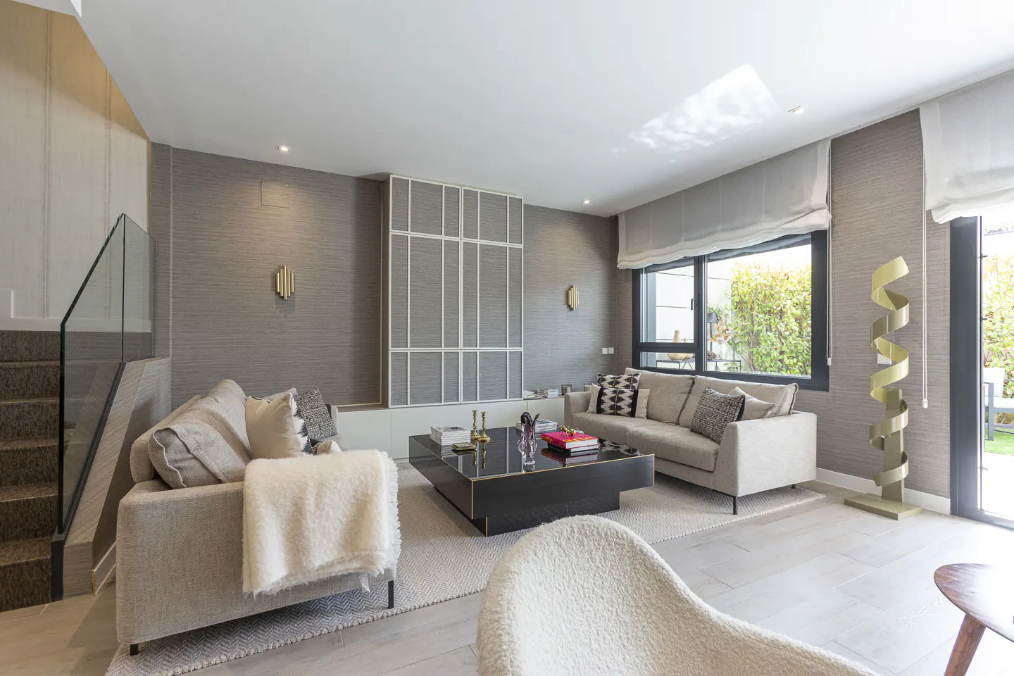 Modern living room with beige sofas, a black coffee table, textured grey walls, and a sculptural gold floor lamp.