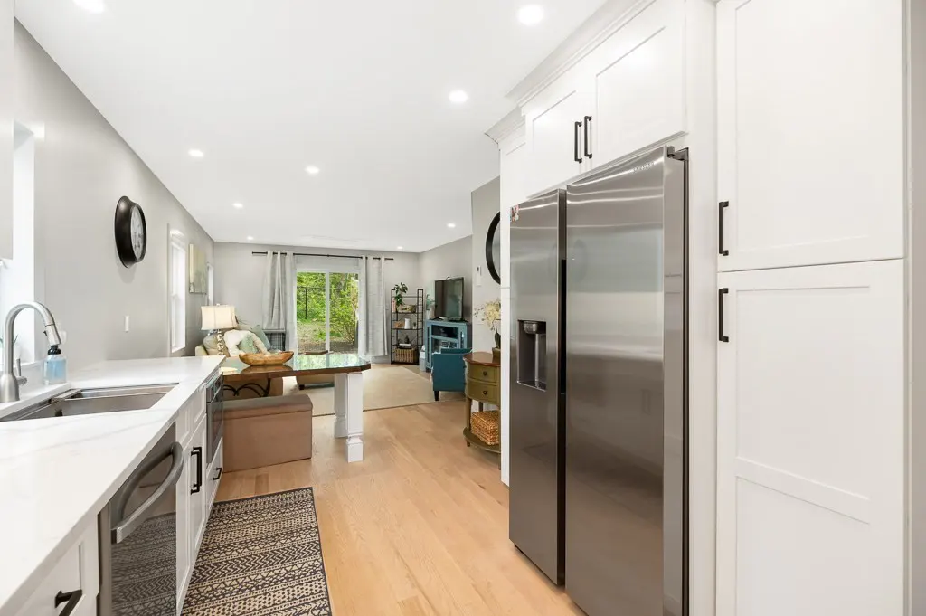 Bright, open-concept kitchen and living room with white cabinets, stainless steel refrigerator, and light wood floors.