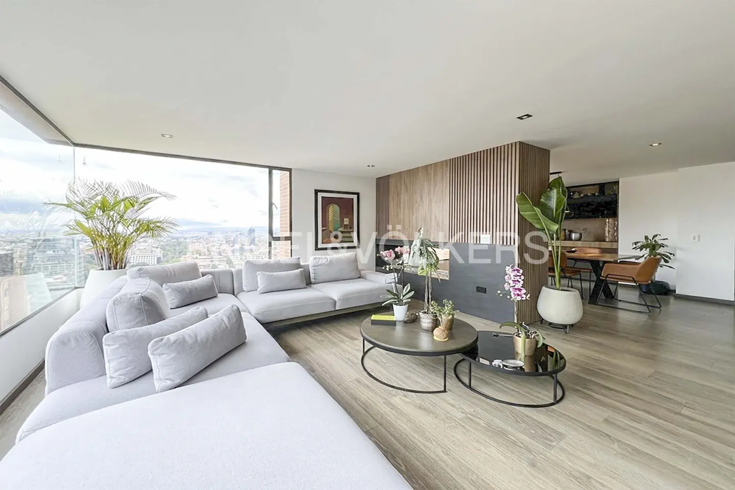 Bright living room with a gray sectional sofa, round coffee tables, and a large window overlooking a city.