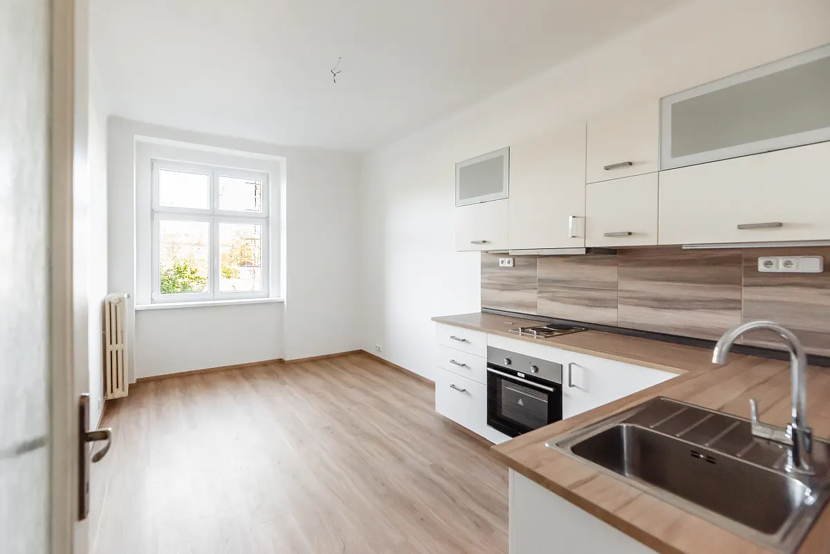 Modern kitchen with white cabinets, wood-look countertops, stainless steel sink, and light wood flooring near a bright window.