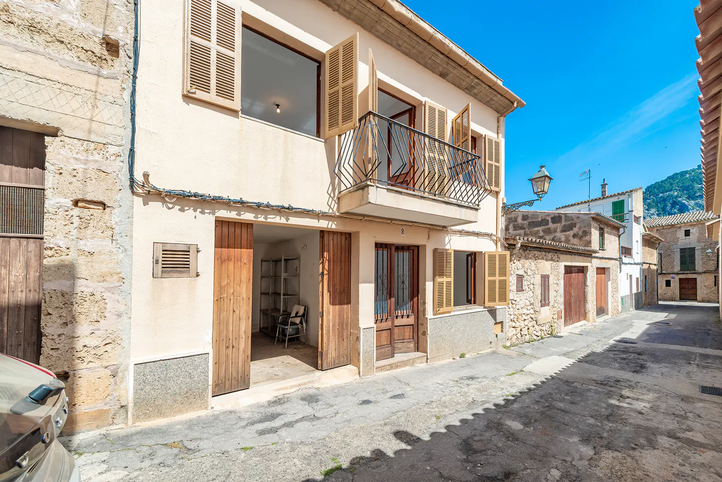 Two-story cream building with a balcony and wooden shutters on a narrow street.