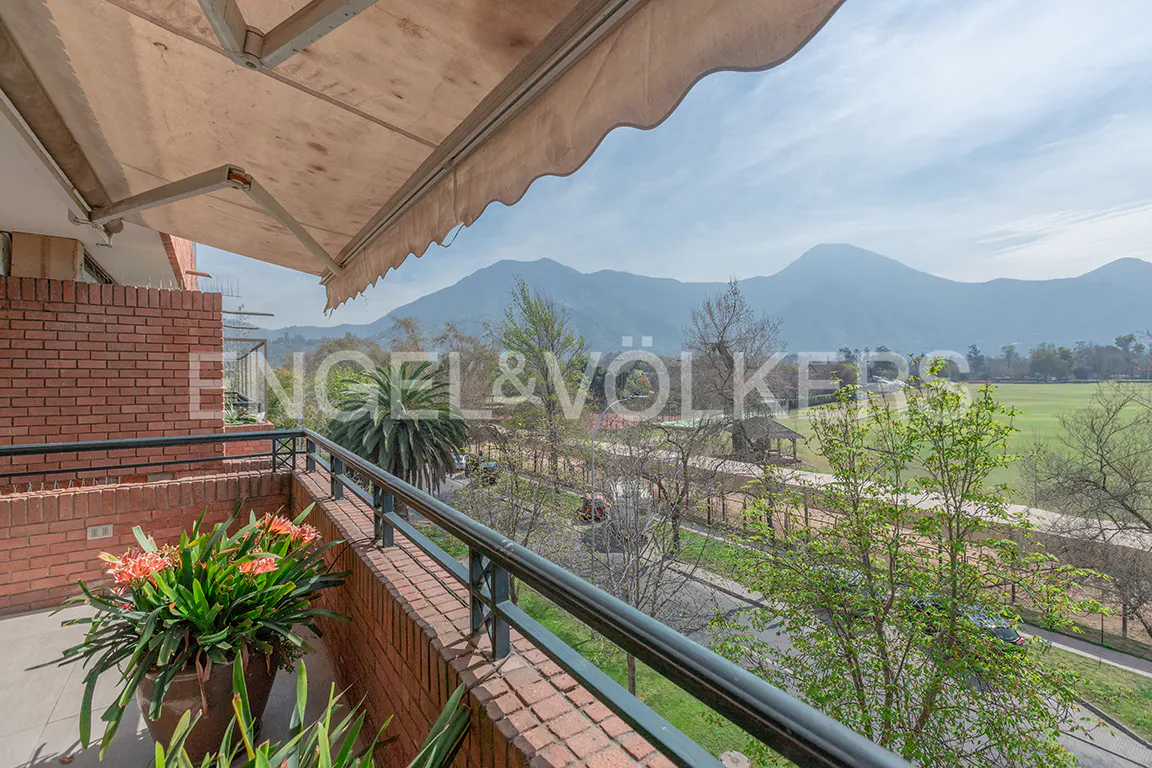 Balcony view with brick railing, potted flowers, and a tan awning. Mountains and trees are visible in the background.