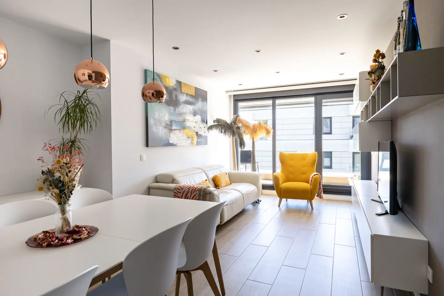 Bright living room with white table and chairs, a white sofa, and a yellow armchair. A large window lets in natural light.