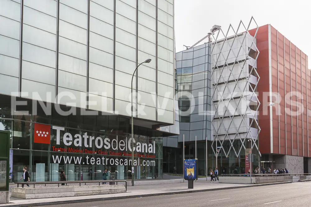 Exterior view of Teatros del Canal, a modern theater complex with glass and red brick facades in Madrid, Spain.