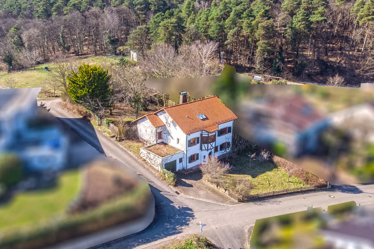 Aerial view of a white house with a red tile roof, brown shutters, and a chimney, surrounded by trees and roads.