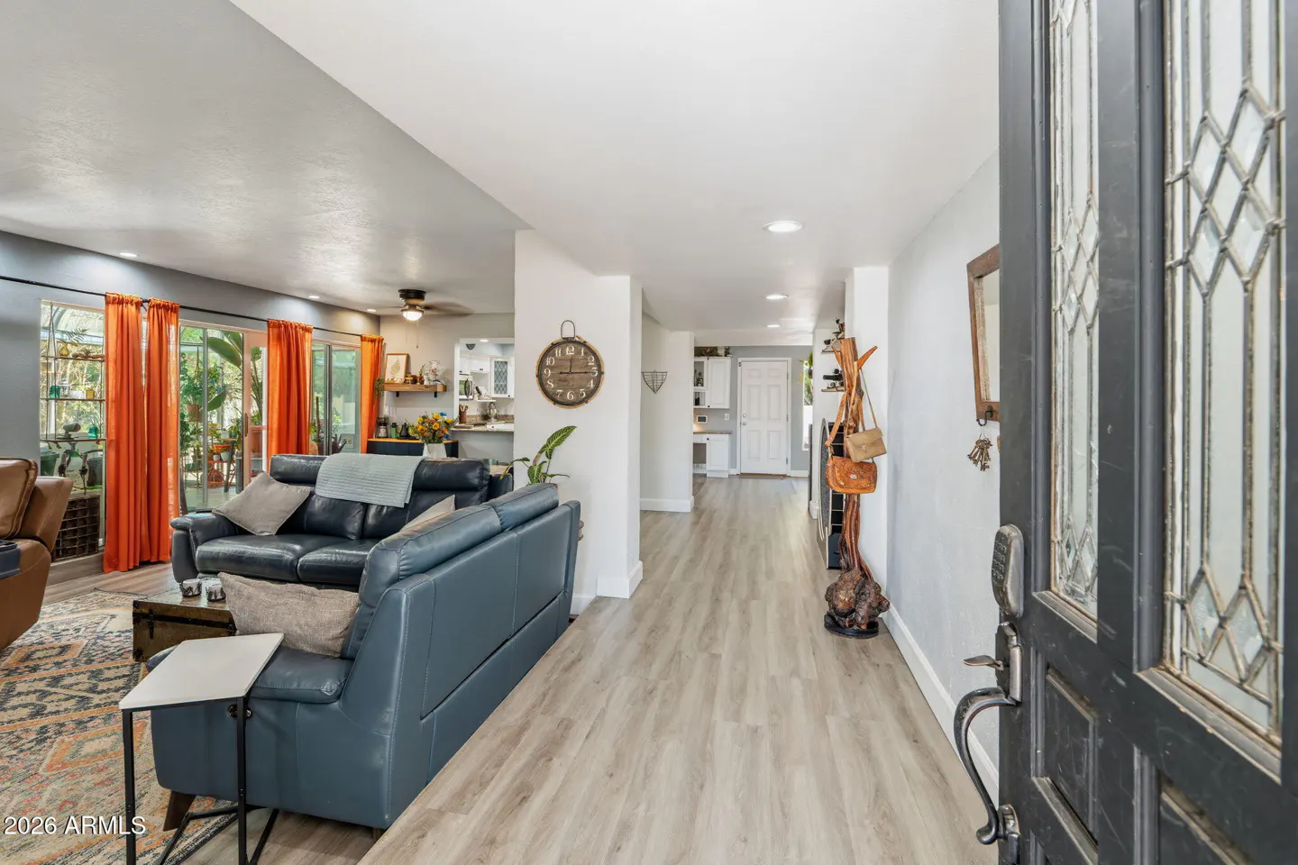 Open front door view of a home's interior with a blue sofa, wood floors, and orange curtains.