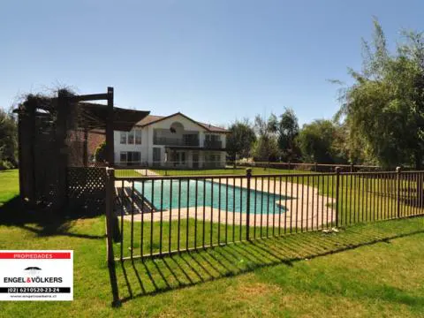 A backyard view of a two-story white house with a pool, surrounded by a brown metal fence and green grass.