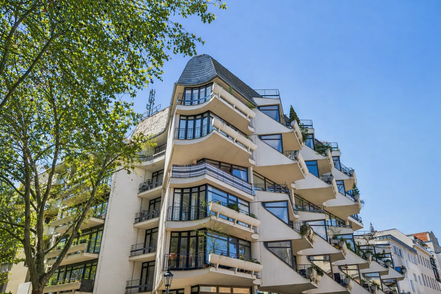 Exterior view of a modern white apartment building with unique balconies and large windows under a clear blue sky.