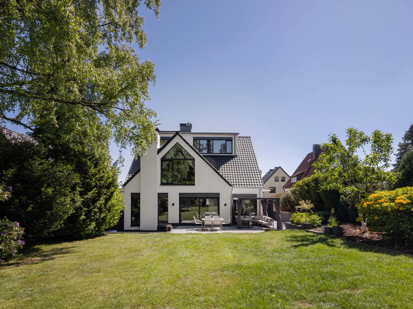 Back view of a modern white house with black trim, a green lawn, and patio furniture.