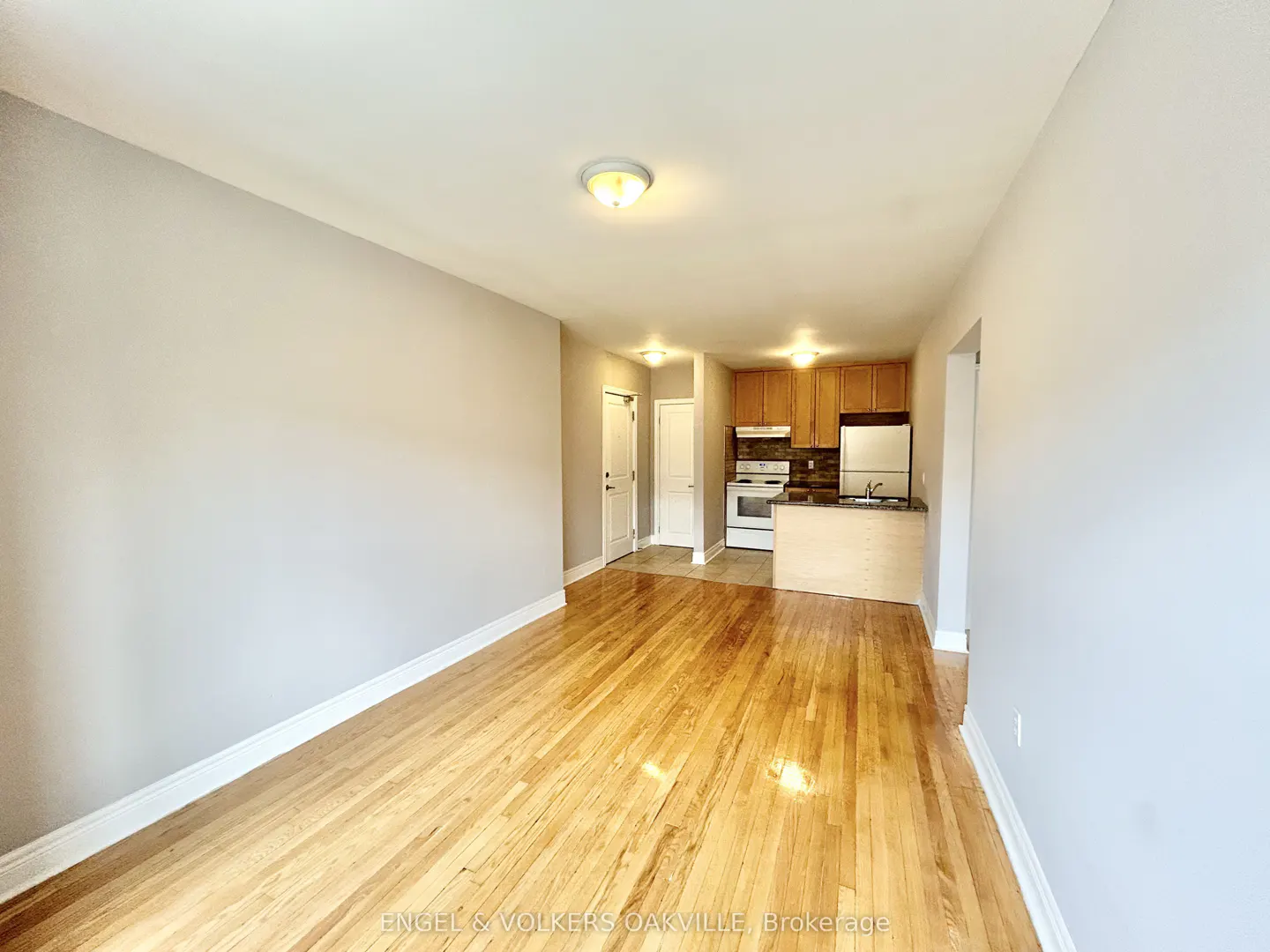 Apartment interior with hardwood floors, light gray walls, and a kitchen with wood cabinets and white appliances.