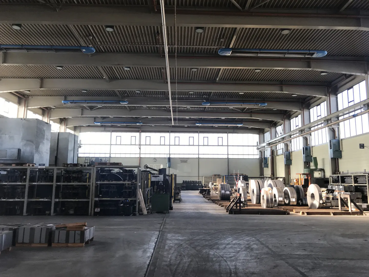 A wide shot of a large, empty warehouse with metal rolls and equipment.